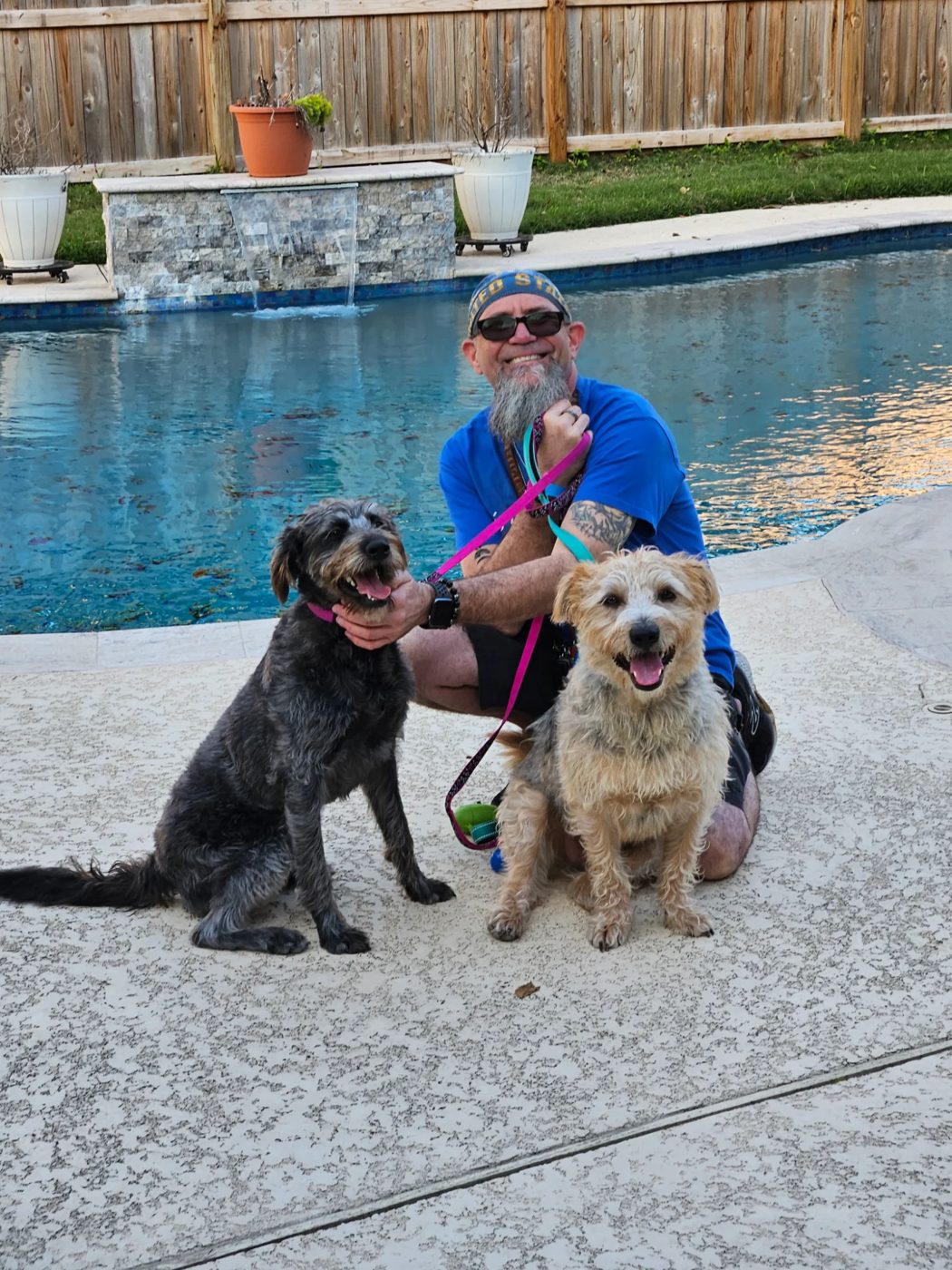 Matt kneeling by a pool with two happy dogs, Ace and Nelly